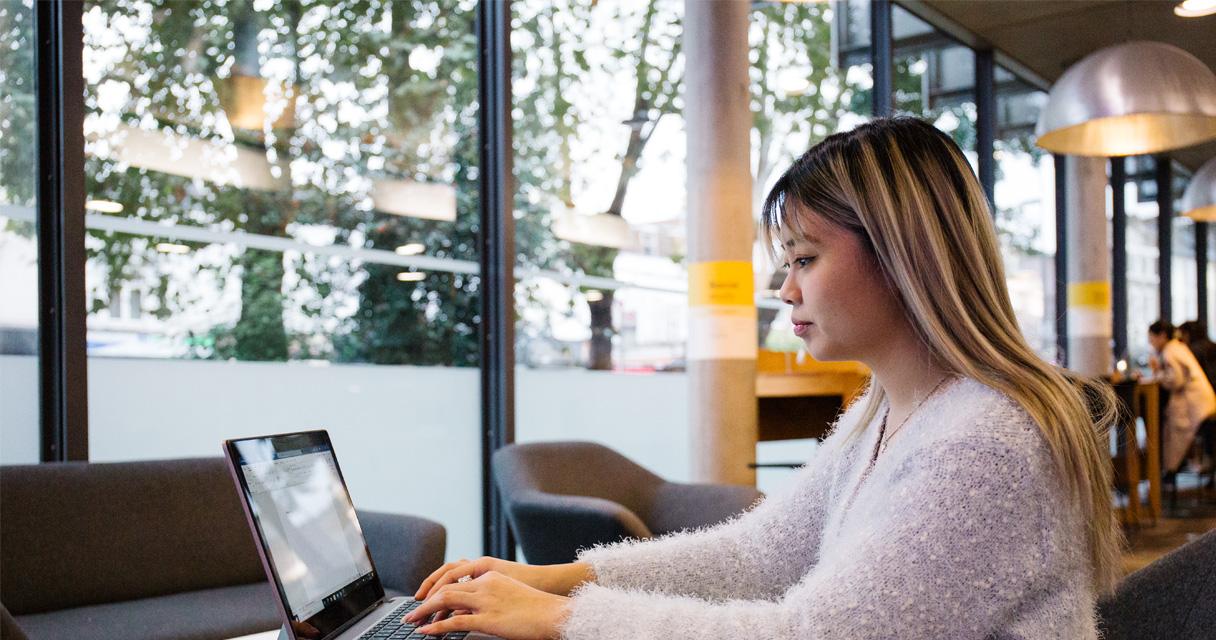 A student works on a laptop in a modern university library.